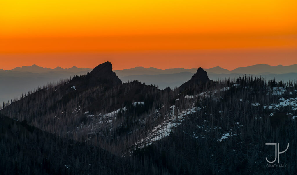 Seemingly endless ridges lie beyond two sharp peaks at sunset